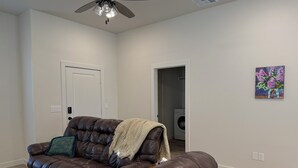 A living room with a brown leather sofa, a ceiling fan, a door, and a washing machine in the background. - Beautiful brand new home. Just entered VRBO market November 6.  All things new! (Lubbock)