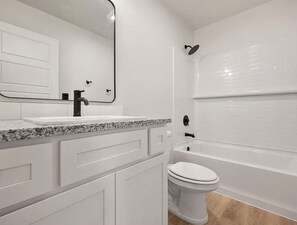A bathroom with a white vanity, a sink, a mirror, a toilet, and a bathtub.