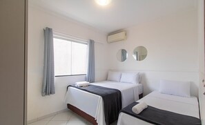 Habitación de hotel con dos camas, una ventana con cortinas, un equipo de aire acondicionado y dos espejos en la pared.