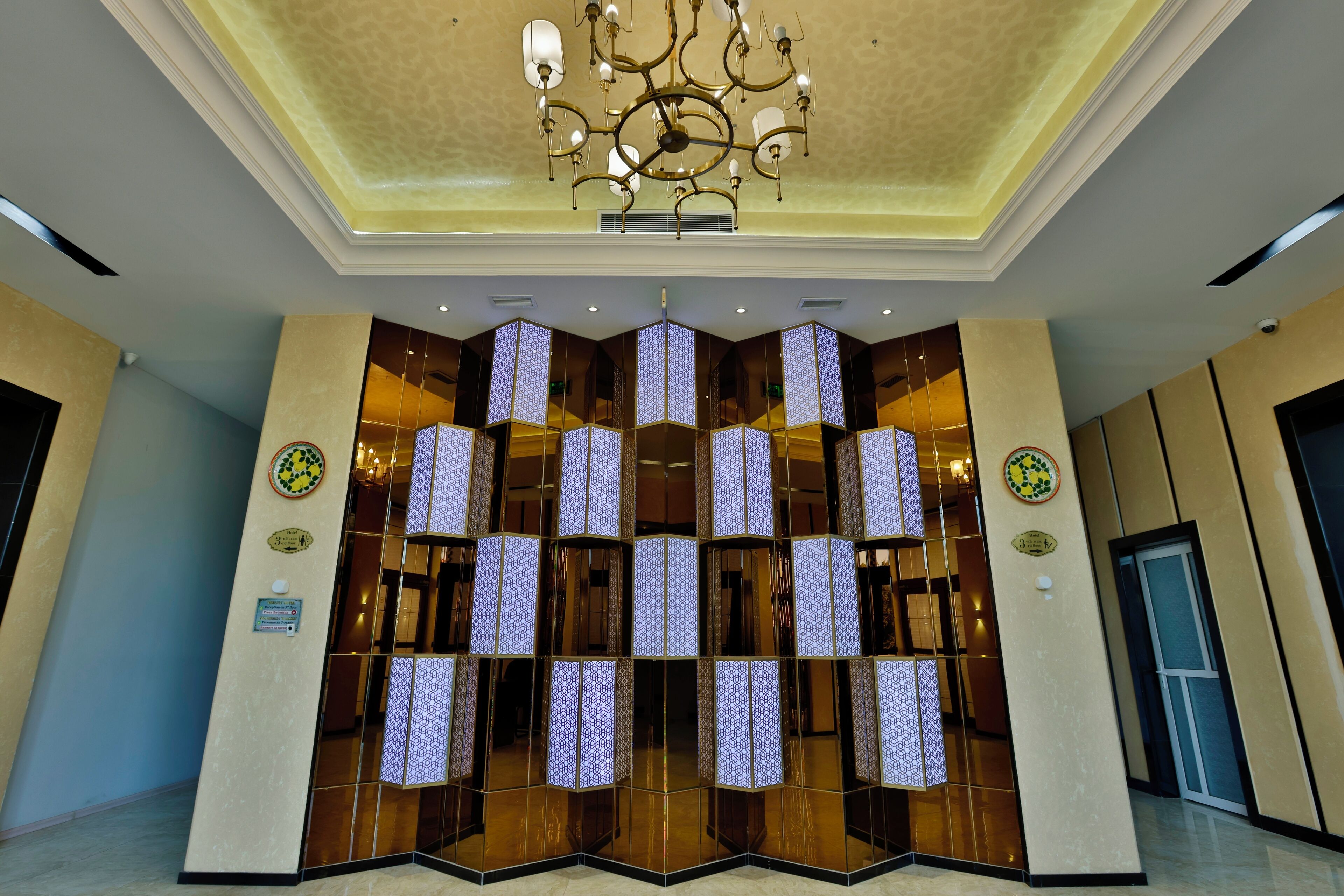 A lobby with a modern chandelier, reflective glass panels, and a polished floor.