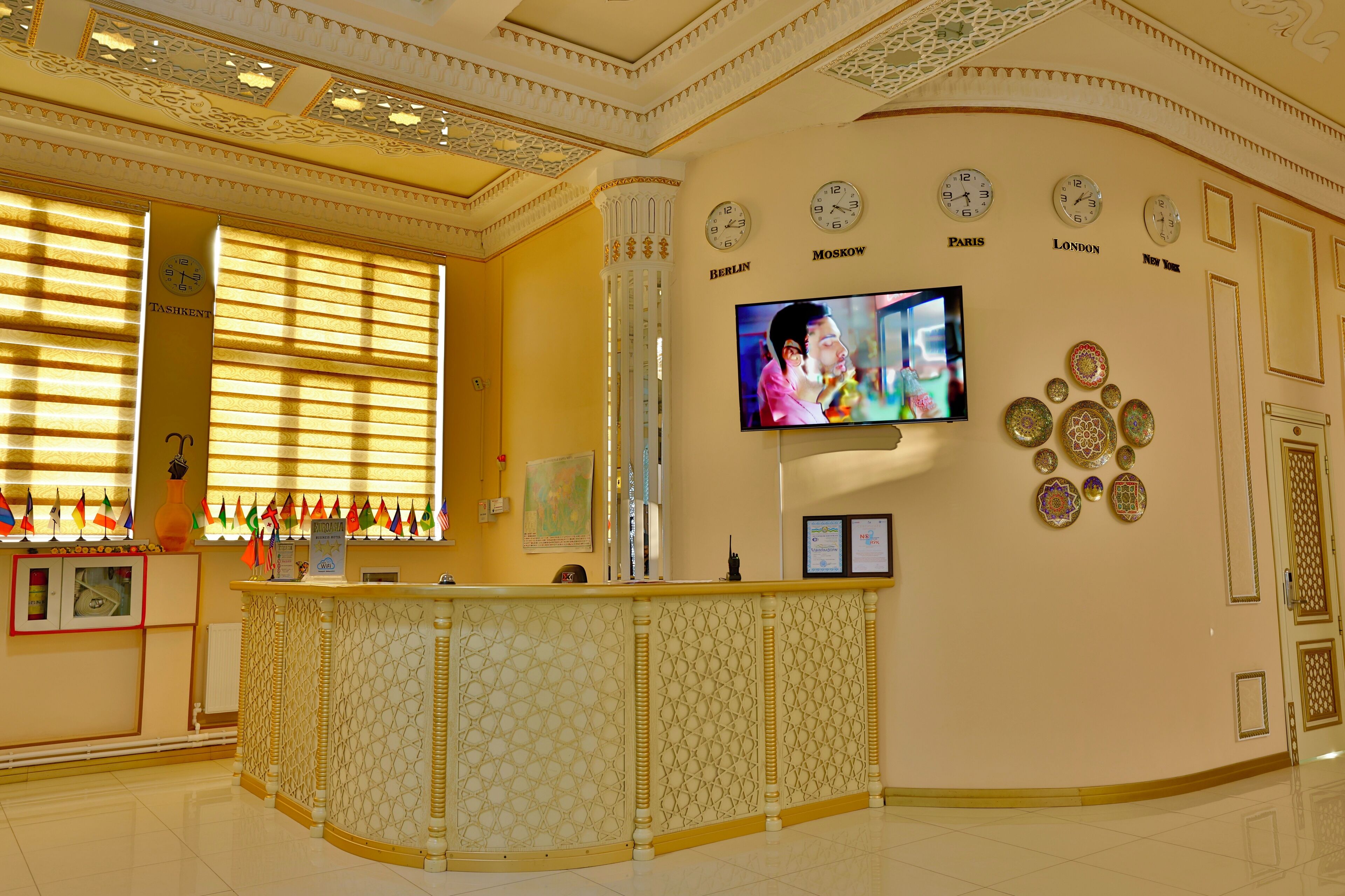 Un'area reception con un bancone, una televisione che mostra una scena e orologi che indicano diverse città.