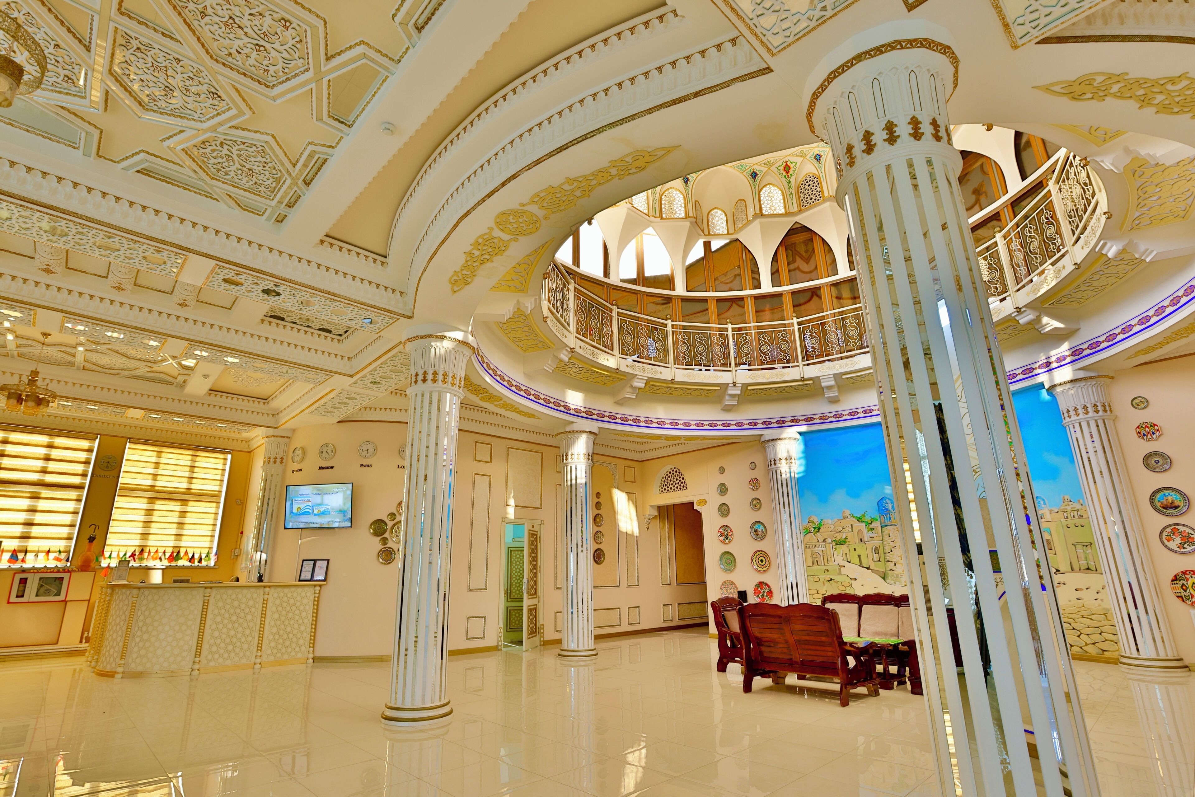A grand lobby with ornate columns, a reception desk, and a balcony with intricate railings.
