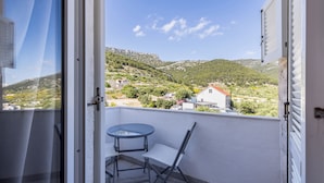 A balcony with a table and chairs, overlooking a hillside with houses and greenery. - Stay @ Bolotel studio SAVE 20 percent on Zlatnirat-bol com (Bol)