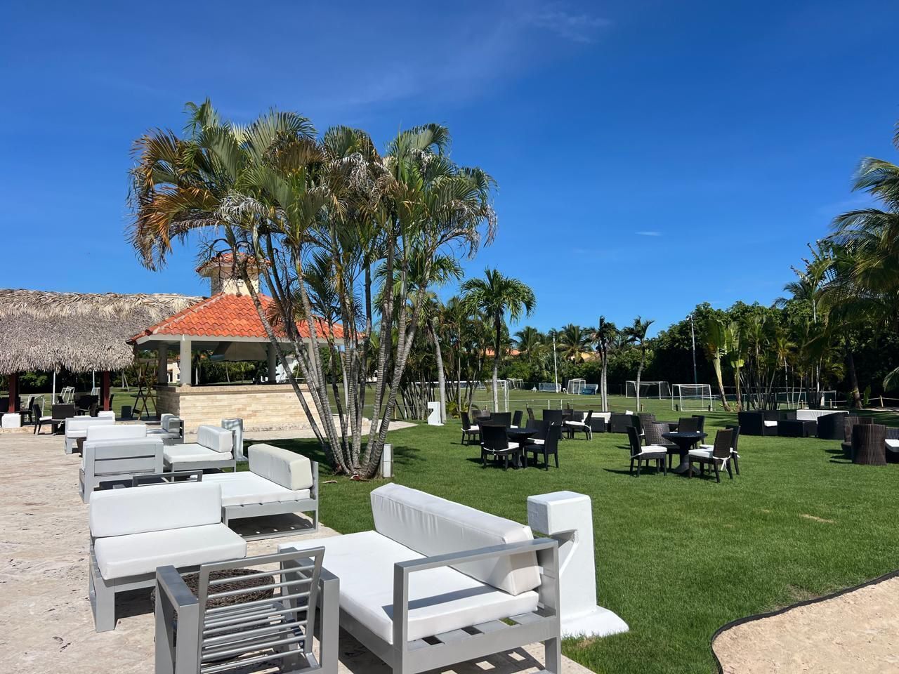 A resort with outdoor seating areas, palm trees, and a thatched-roof structure.