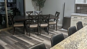A modern kitchen with a dining area, featuring a granite countertop, a dining table with chairs, and a hanging light fixture. - Game Room • New Construction • 5 Bedrooms, 2 Baths (Mesquite)