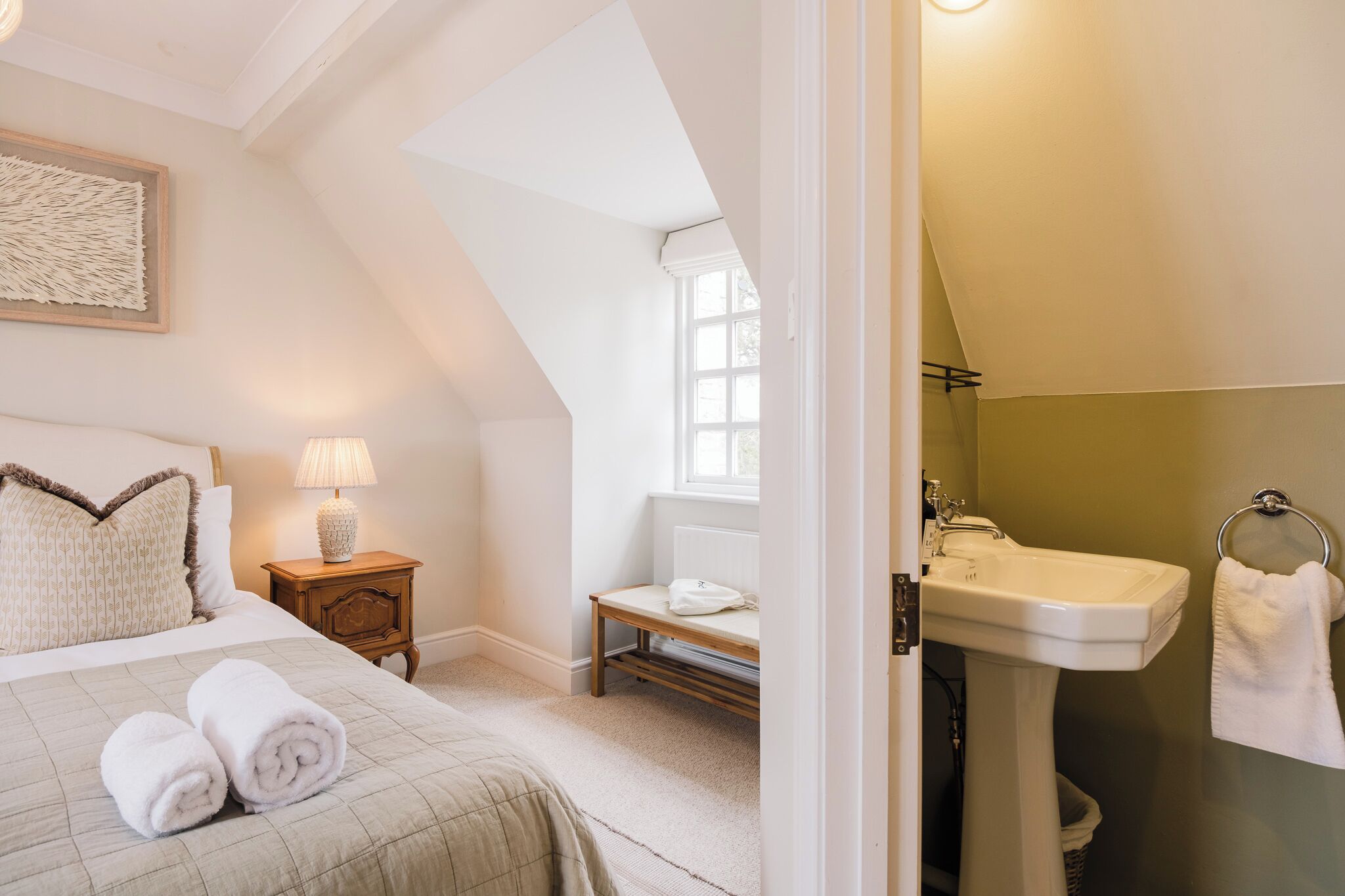 A bedroom with a bed, bedside lamp, and a view of a window.