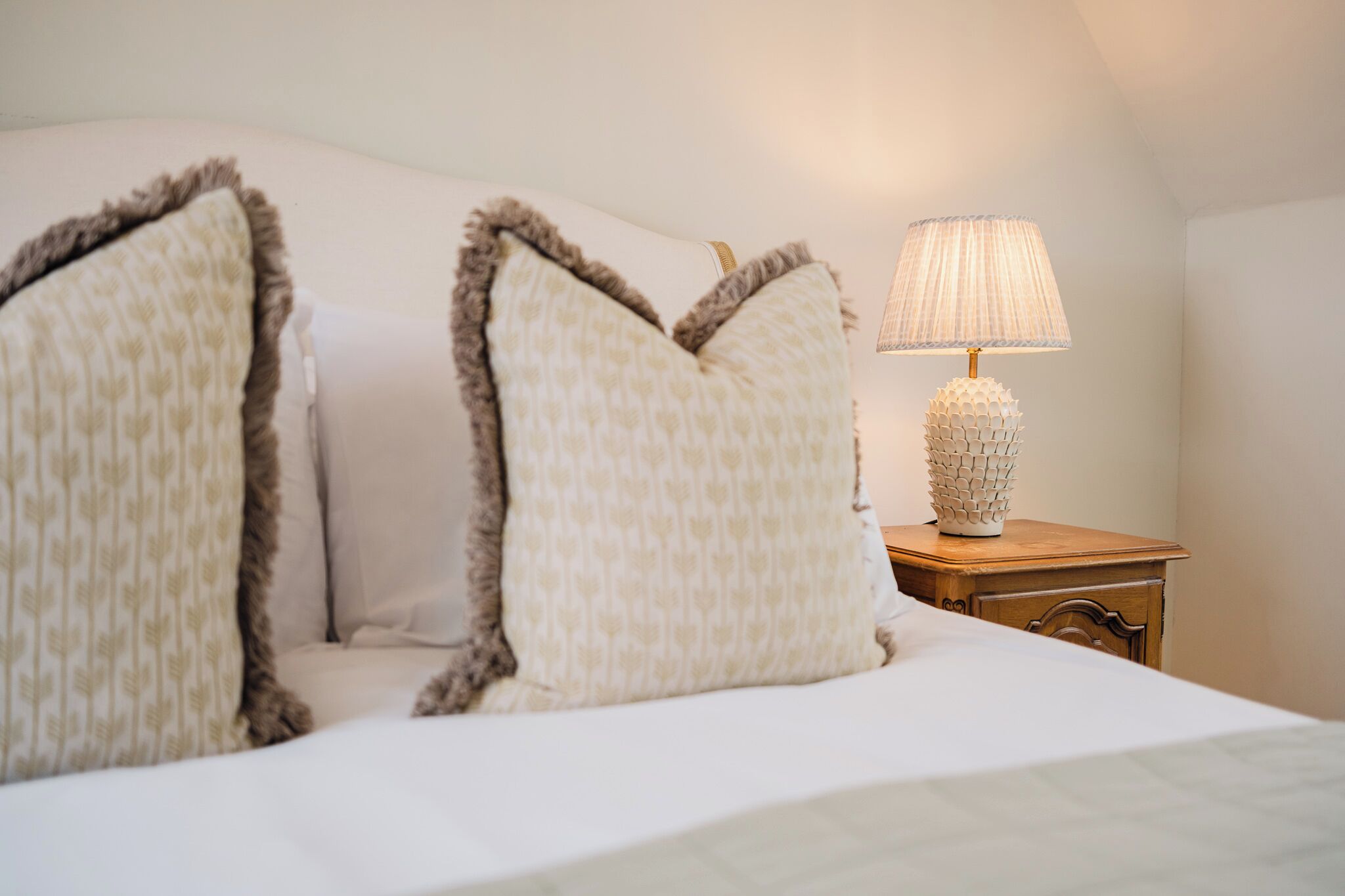 A neatly made bed with two large pillows and a decorative lamp on a wooden nightstand.