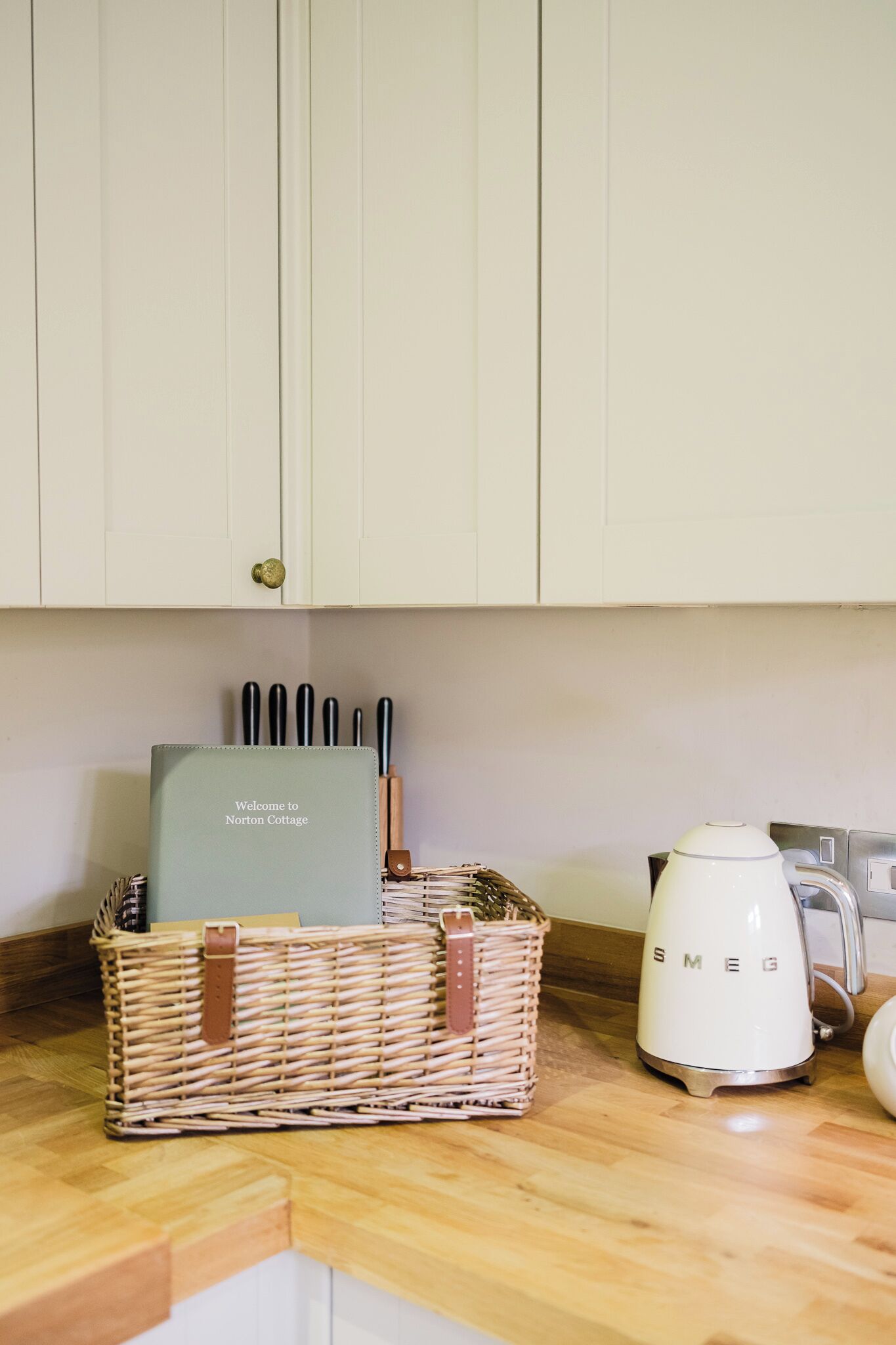 A kitchen with a wicker basket containing a welcome booklet and utensils, a white electric kettle, and a toaster.