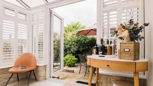 Una veranda con una sedia, un tavolino in legno e vista su un giardino.