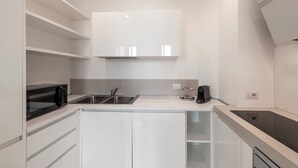 Een moderne keuken met witte kasten, een zwarte magnetron, een spoelbak en een ingebouwde kookplaat.