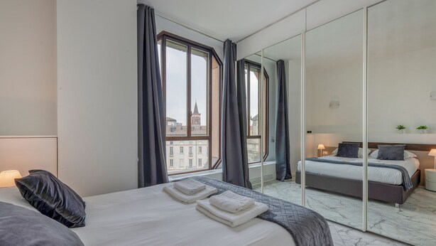 Een moderne hotelkamer met een groot bed, een spiegel en uitzicht op een stadsgezicht.