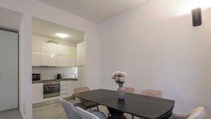 Een moderne eetruimte met een donkere tafel, zes grijze stoelen, een vaas met bloemen en een keuken op de achtergrond.