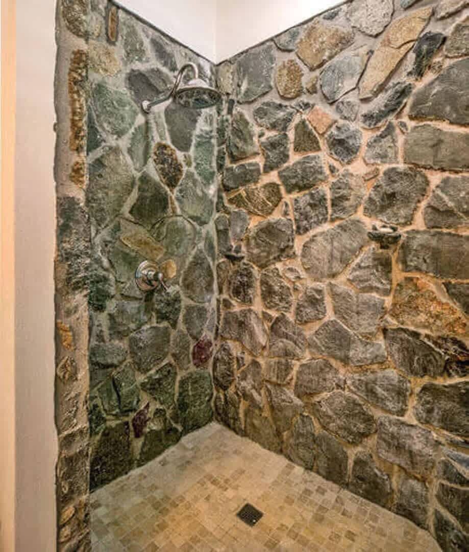 Une douche aux murs en pierre, dotée d  ’un pommeau de douche à effet pluie et d’un drain.