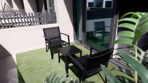 Ein Balkon mit einem grünen Kunstrasenteppich, zwei schwarzen Stühlen und einem Glastisch.