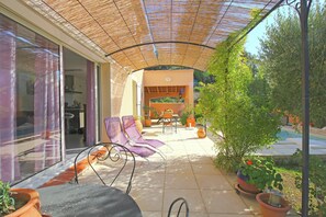 A covered patio with a table and chairs, potted plants, and a view of a swimming pool.