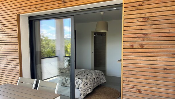A modern bedroom with a bed, a sliding glass door leading to a balcony, and a dining area with a table and chairs.