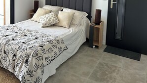 A modern bedroom with a large bed, a dark headboard, bedside tables, a lamp, and a door.