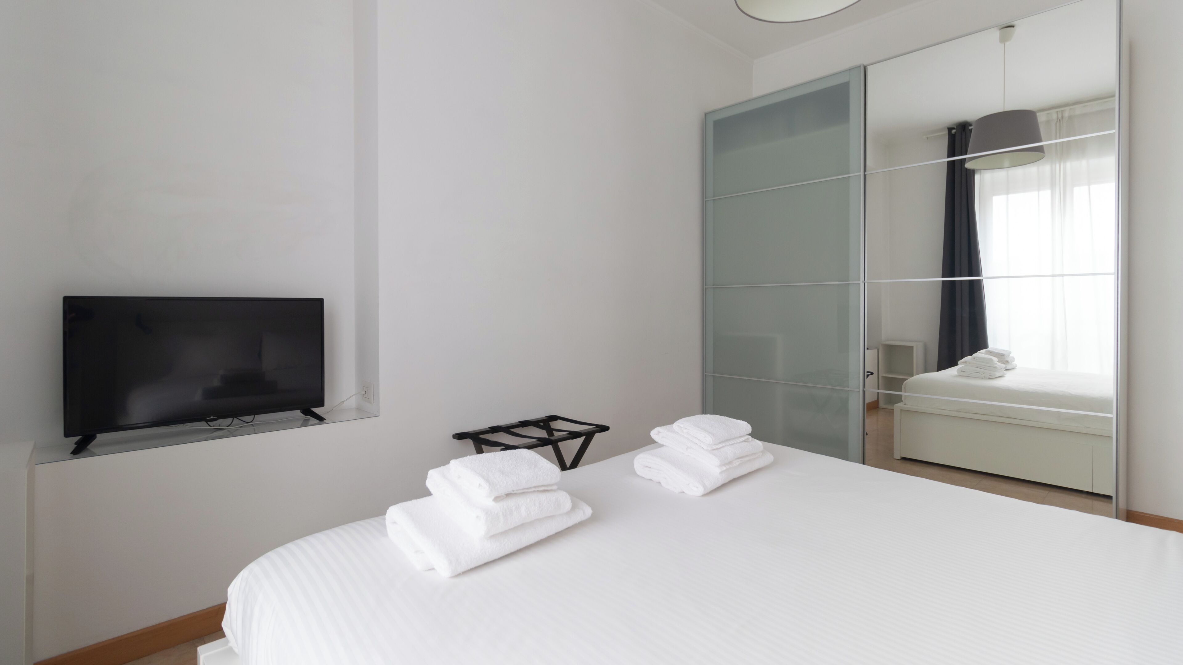 A hotel room with a bed, a TV, a wardrobe, and a window with curtains.