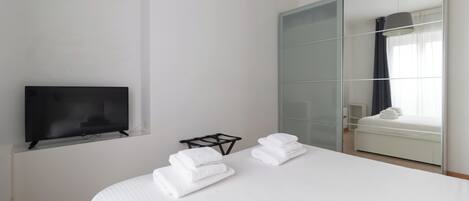 A hotel room with a bed, a TV, a wardrobe, and a window with curtains.