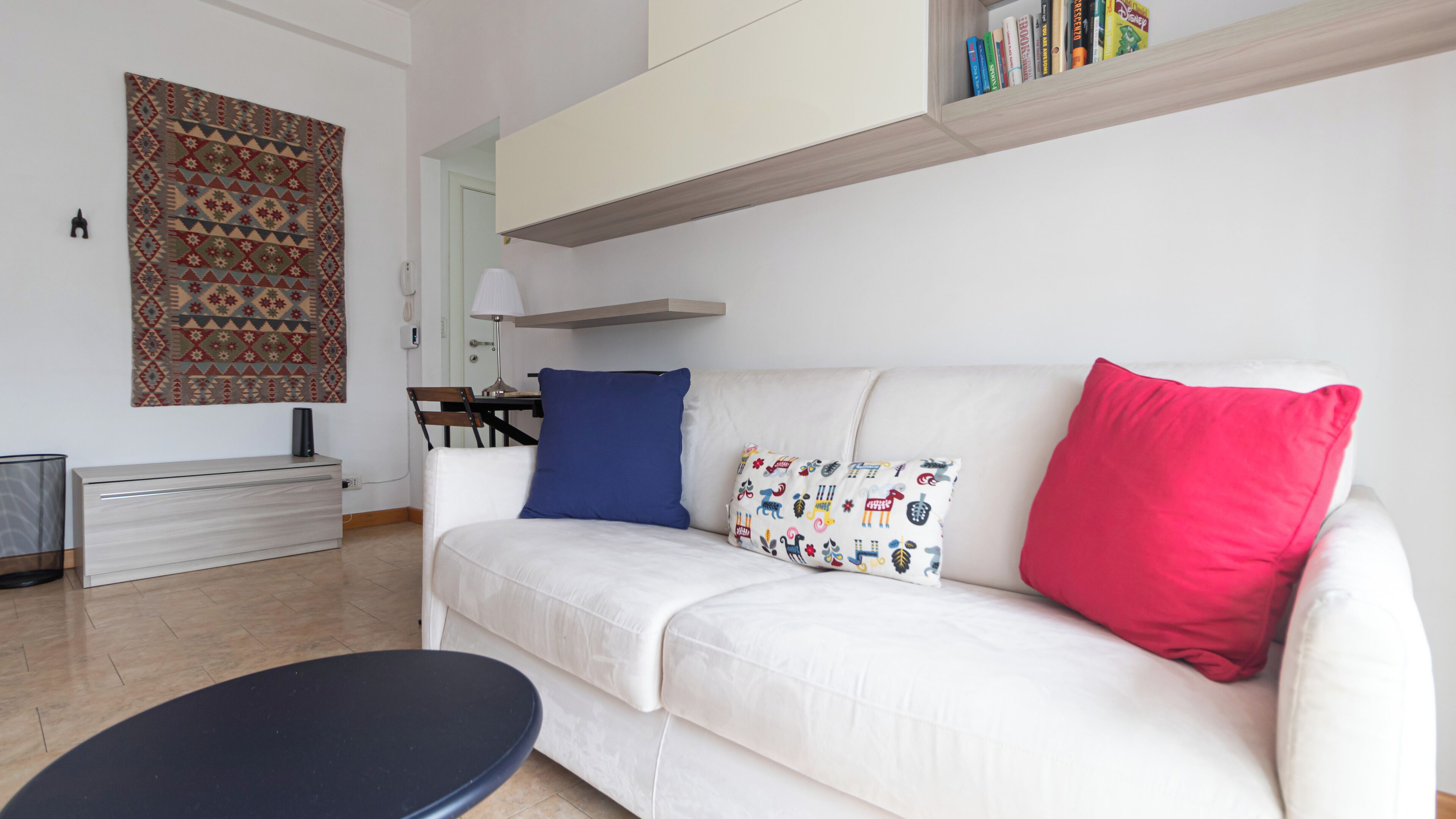 Una sala de estar moderna con un sofá blanco, un tapete estampado, una mesita y una estantería con libros.