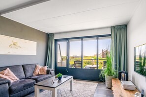 Een moderne woonkamer met een donkergrijze bank, een houten salontafel en een groot raam met gordijnen.
