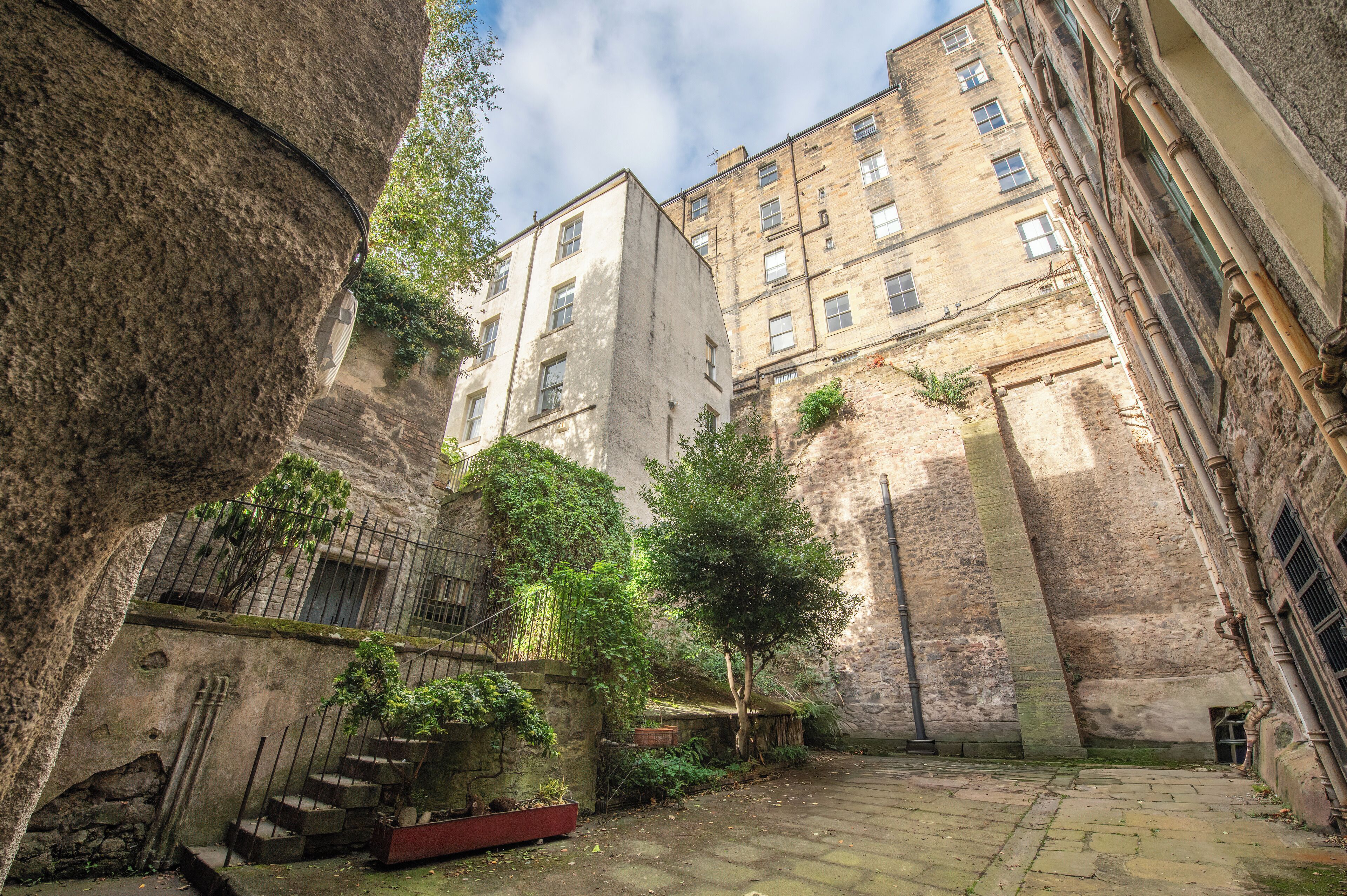 A narrow alleyway with stone walls, a staircase, and a small garden area with trees.