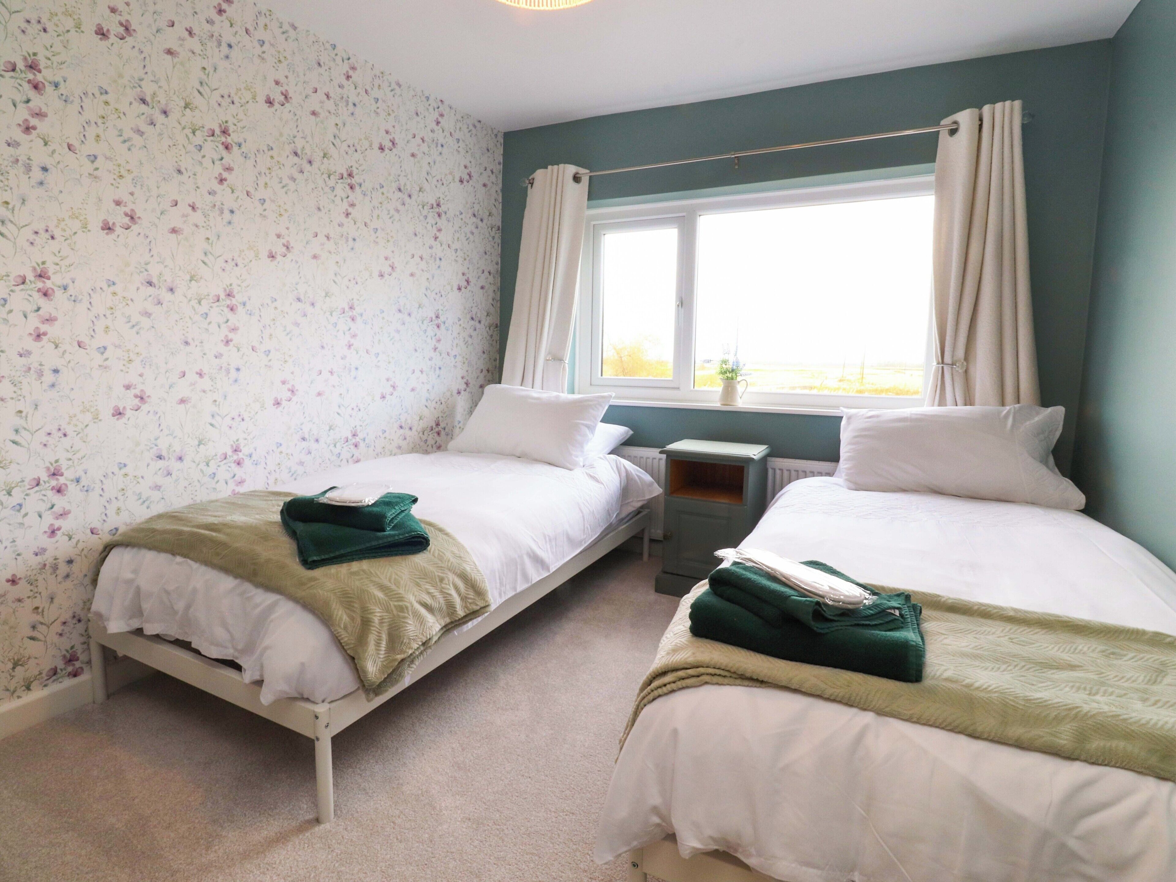 A bedroom with two single beds, a nightstand, a window with curtains, and floral wallpaper.