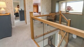 Une pièce spacieuse avec un escalier en bois, donnant sur la cuisine, et une fenêtre ornée de fleurs.