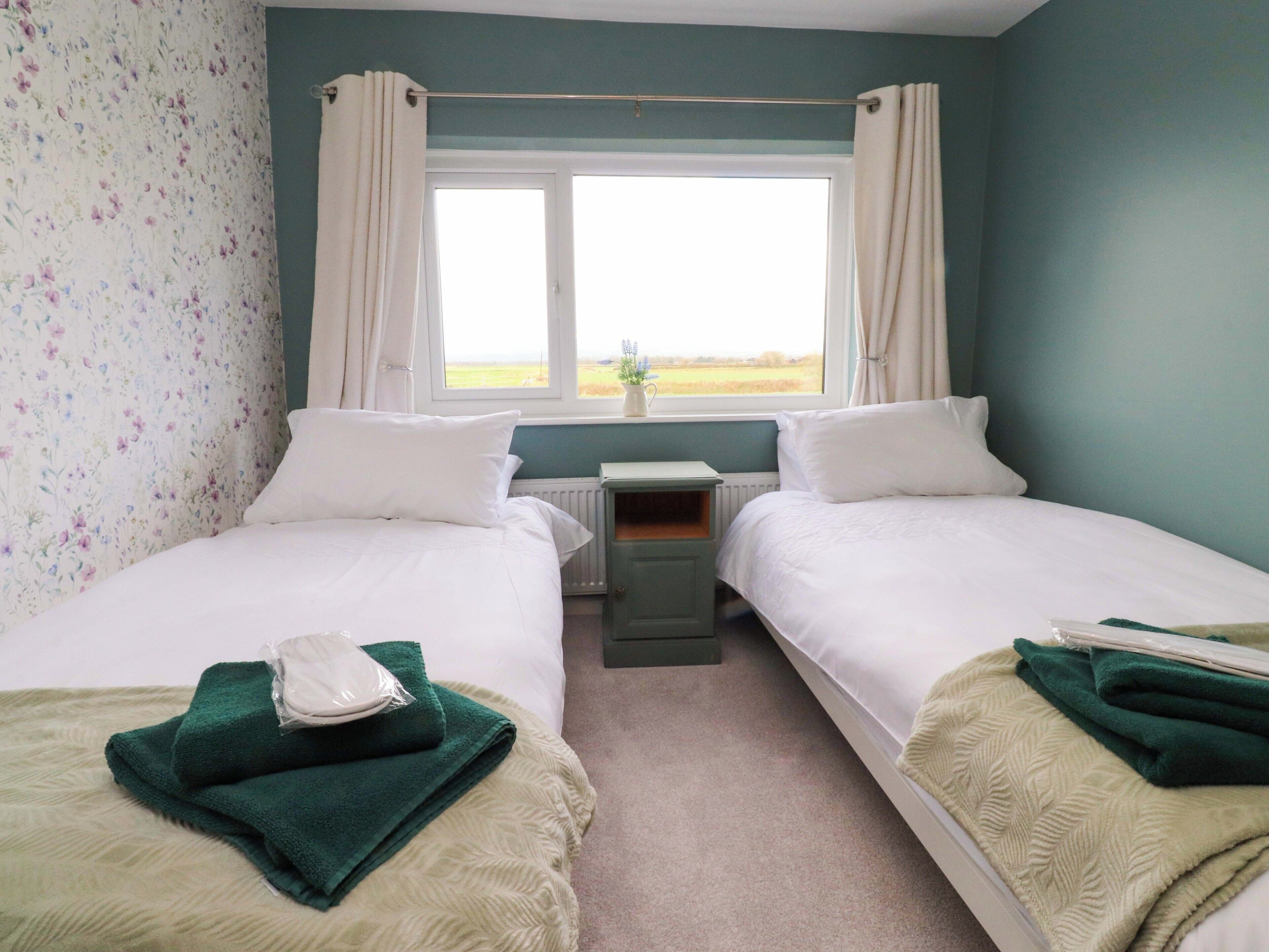 A twin room with two beds, a window with curtains, a radiator, and a small table.