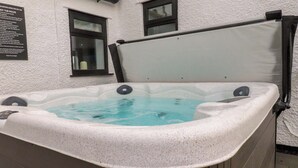 Un bain à remous à l’extérieur blanc, placé contre un mur blanc percé de deux fenêtres.