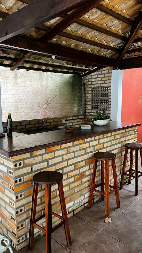 A kitchen area with a brick counter, stools, and a hanging light fixture. - Pousada Sol de Maria (Tibau do Sul)