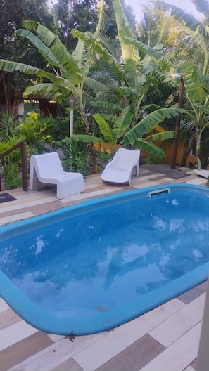 A swimming pool with two white lounge chairs and a tiled deck. - Pousada Sol de Maria (Tibau do Sul)