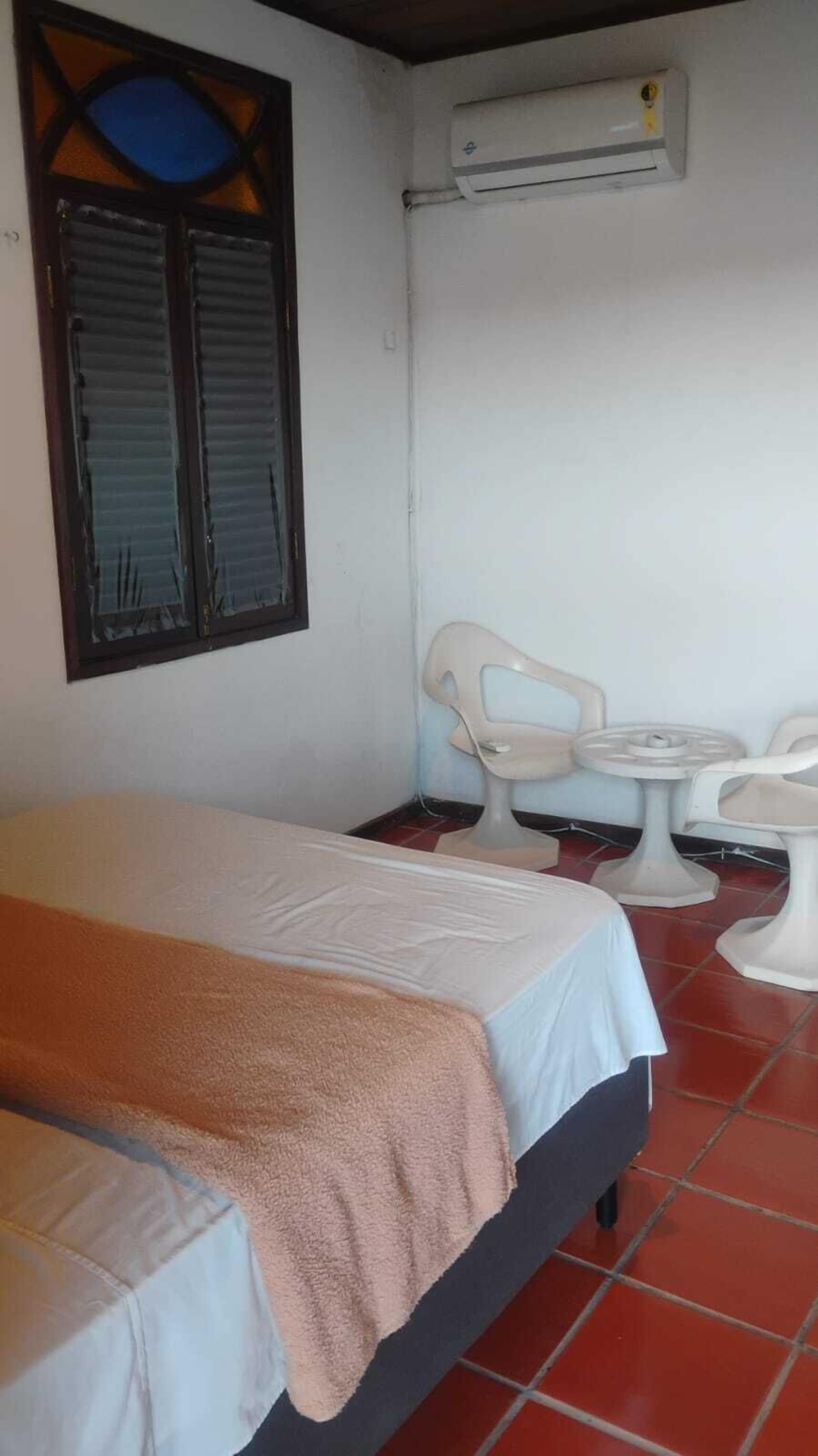 Una stanza con un letto, due sedie, un tavolino e un condizionatore.