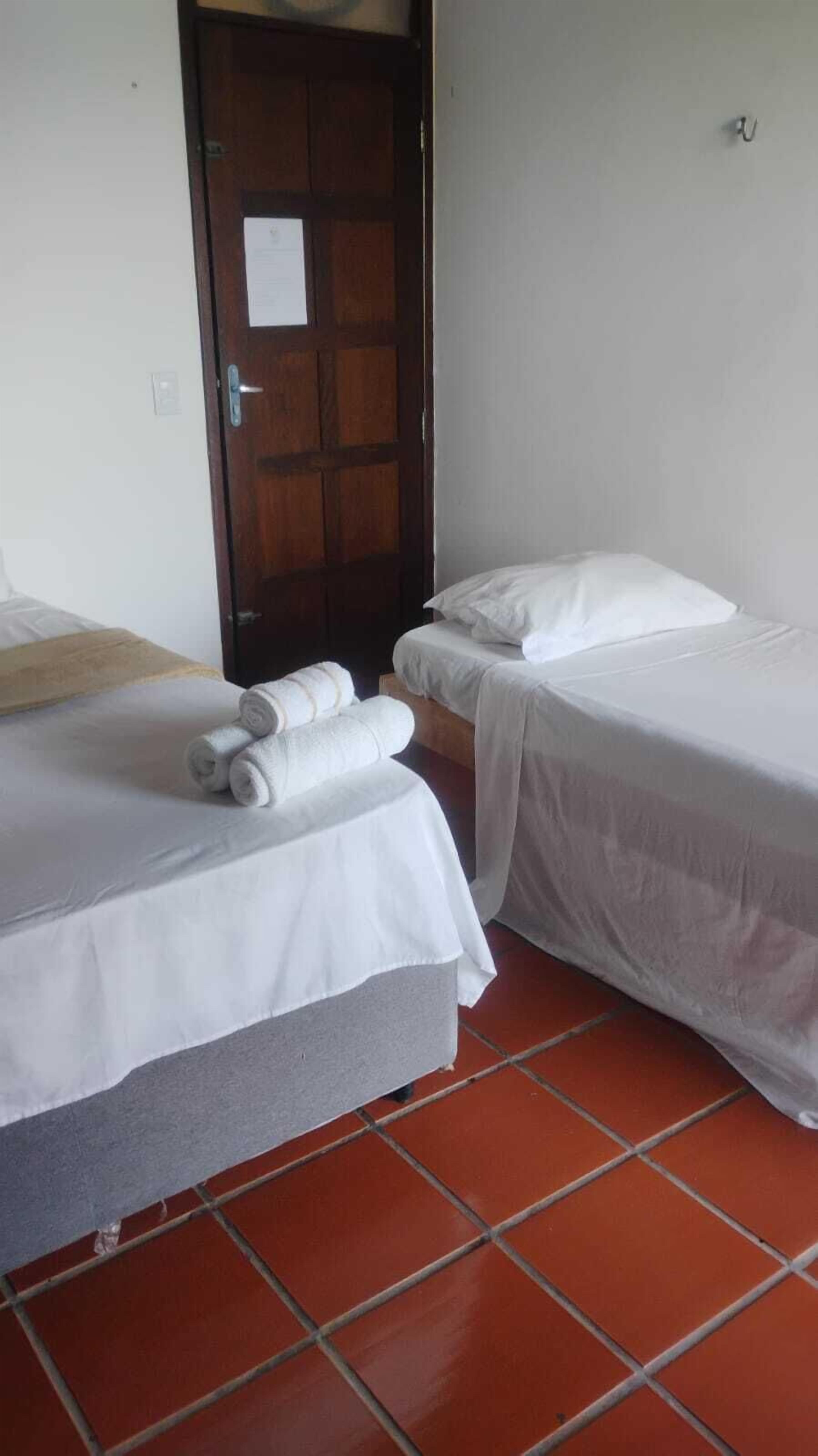 Une chambre d’hôtel avec deux lits simples, une porte en bois et un sol carrelé.