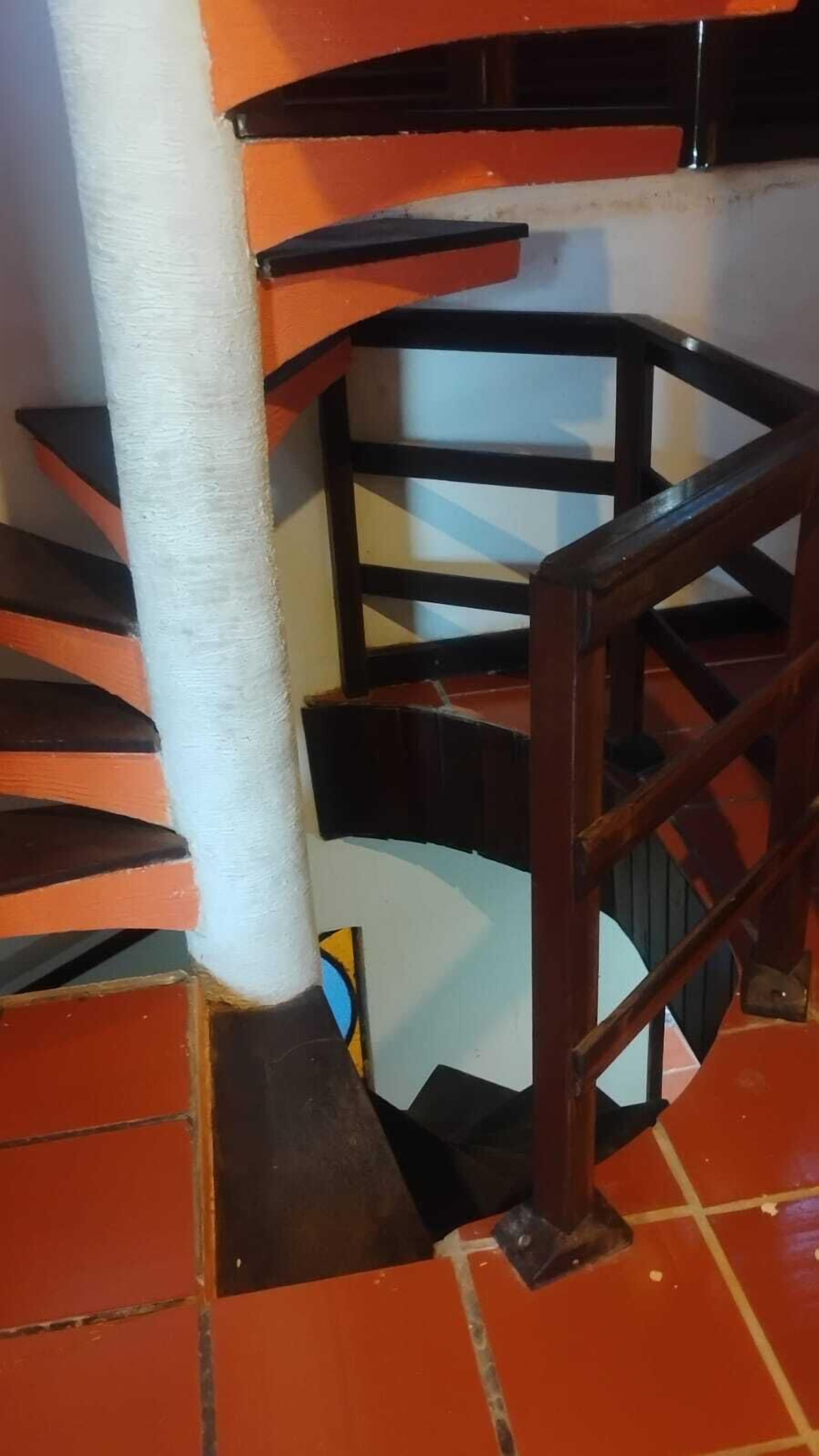 A spiral staircase with a white handrail and black steps, leading to a lower level.