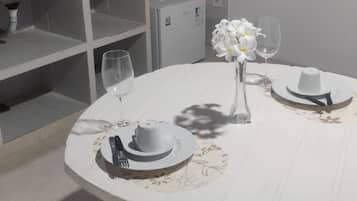 A round dining table with a white tablecloth, two white plates, a vase with white flowers, and two wine glasses.