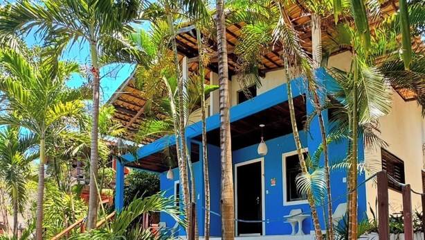 Un edificio blu con un tetto di paglia, circondato da palme e terreno sabbioso.