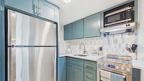 Una cocina con un refrigerador de acero inoxidable, un microondas, una cafetera y una estufa.