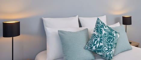 Una cama bien hecha con almohadas blancas y estampadas, dos lámparas de noche negras y una mesita de noche de madera.