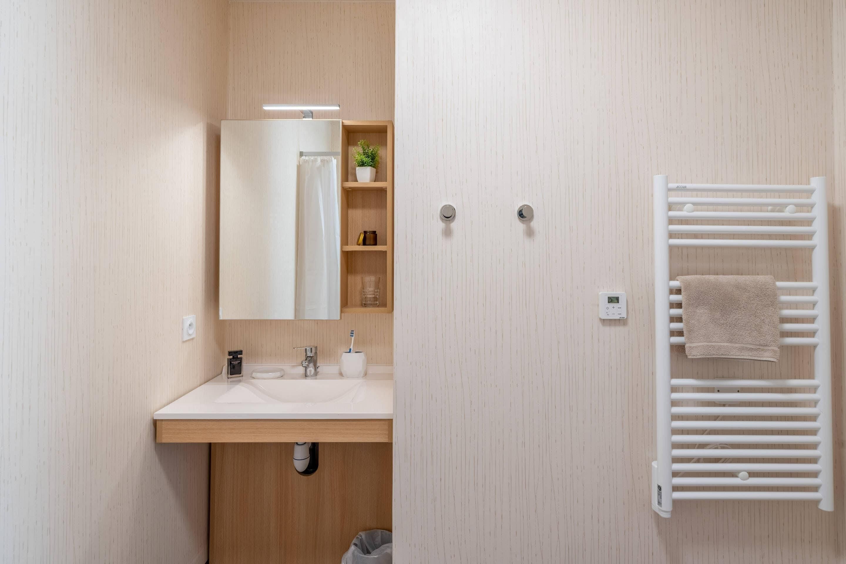 Une salle de bain moderne avec un meuble-lavabo en bois, un miroir, un porte-serviettes et une petite étagère contenant des articles de toilette.