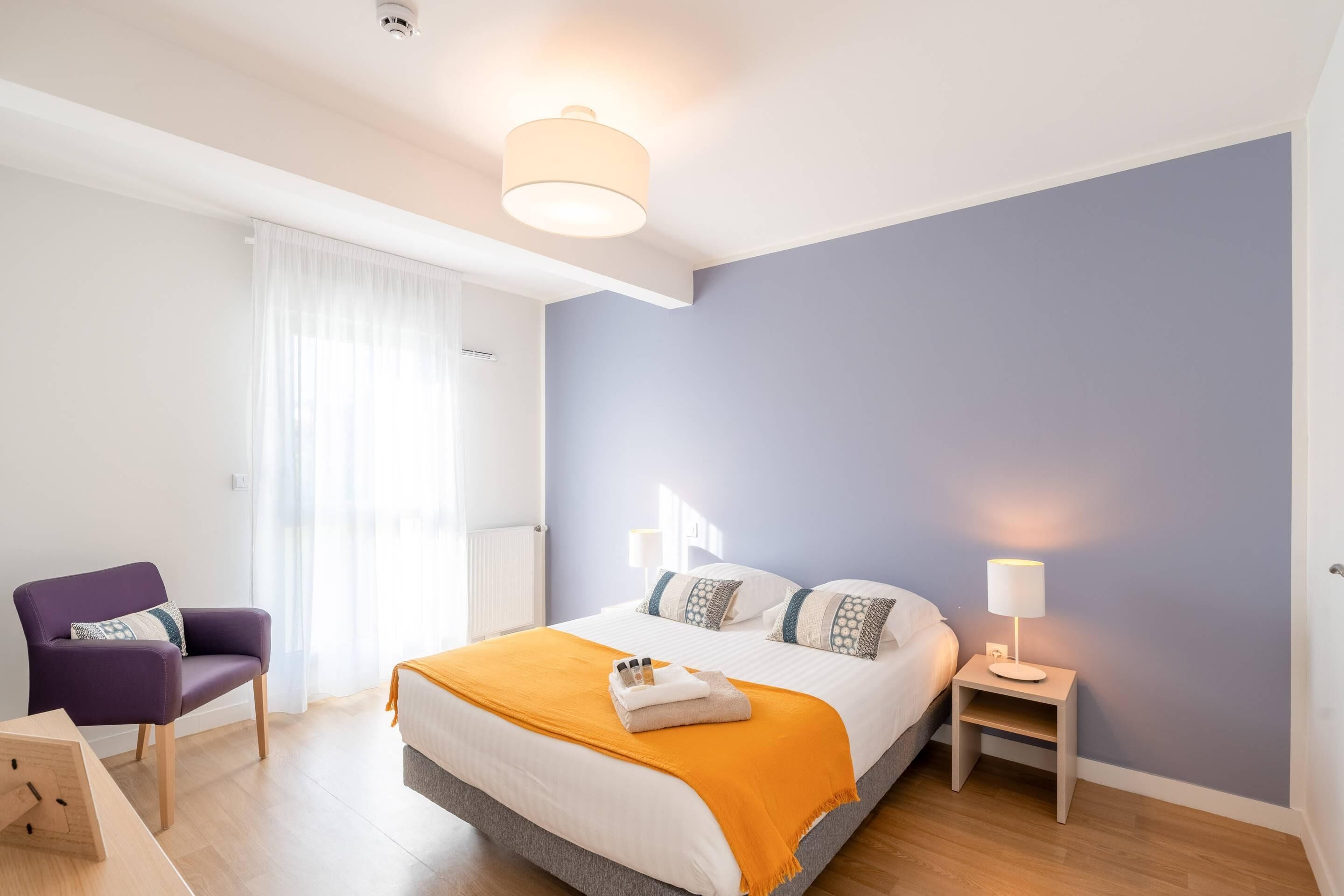Ein modernes Schlafzimmer mit Bett, Stuhl, Nachttisch und Lampe.