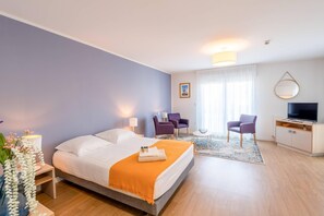 A modern hotel room with a large bed, a desk with a TV, two purple armchairs, and a small table with a bowl. - Quality Aparthotel Rochefort (Rochefort)