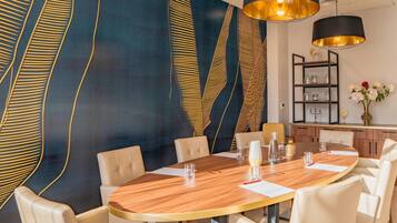 A modern dining area with a round wooden table, white upholstered chairs, and a decorative wall with abstract patterns.
