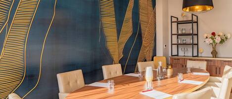 A modern dining area with a round wooden table, white upholstered chairs, and a decorative wall with abstract patterns.
