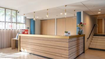 Un espace d’accueil doté d’un comptoir de réception en bois, d’un éclairage suspendu, d’un escalier et offrant une vue sur l’extérieur.