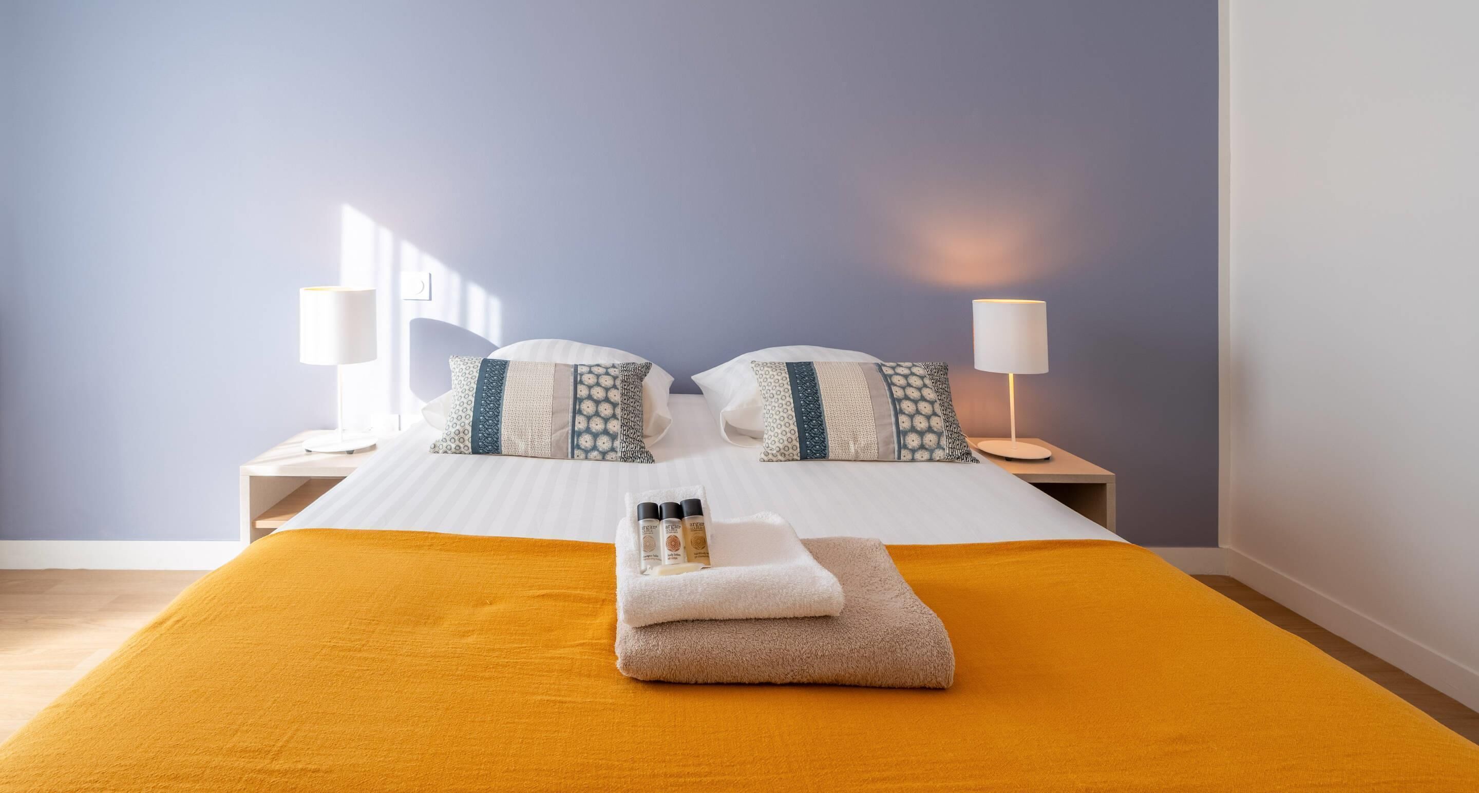 Ein Hotelzimmer mit Bett, zwei Nachttischen, einer Lampe und einem Fenster.