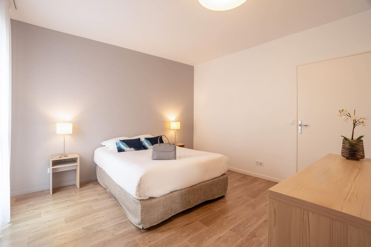 A bedroom with a bed, bedside tables, a nightstand, a wooden dresser, and a potted plant.