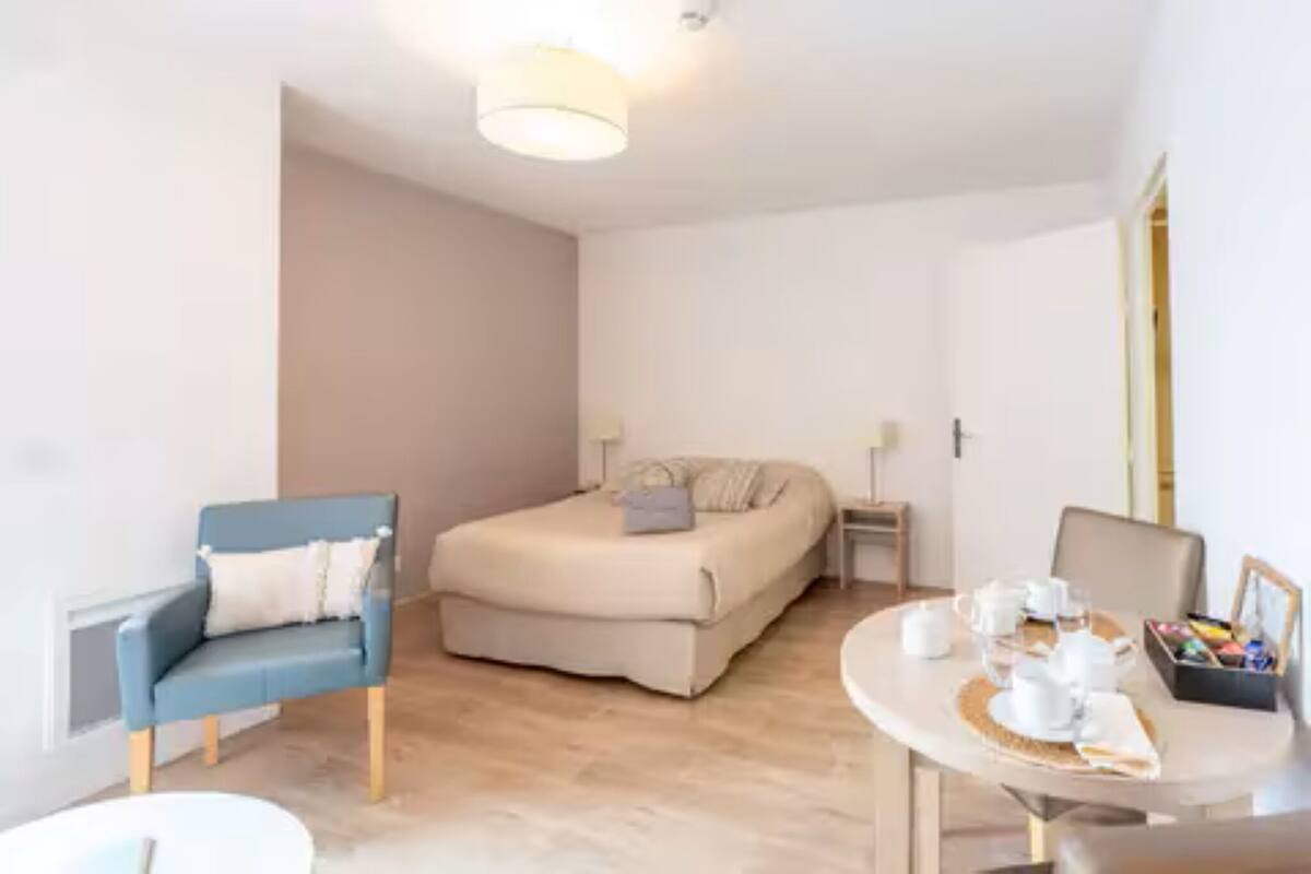 A bedroom with a bed, a chair, a bedside table with a lamp, and a dining area with a table set for breakfast.