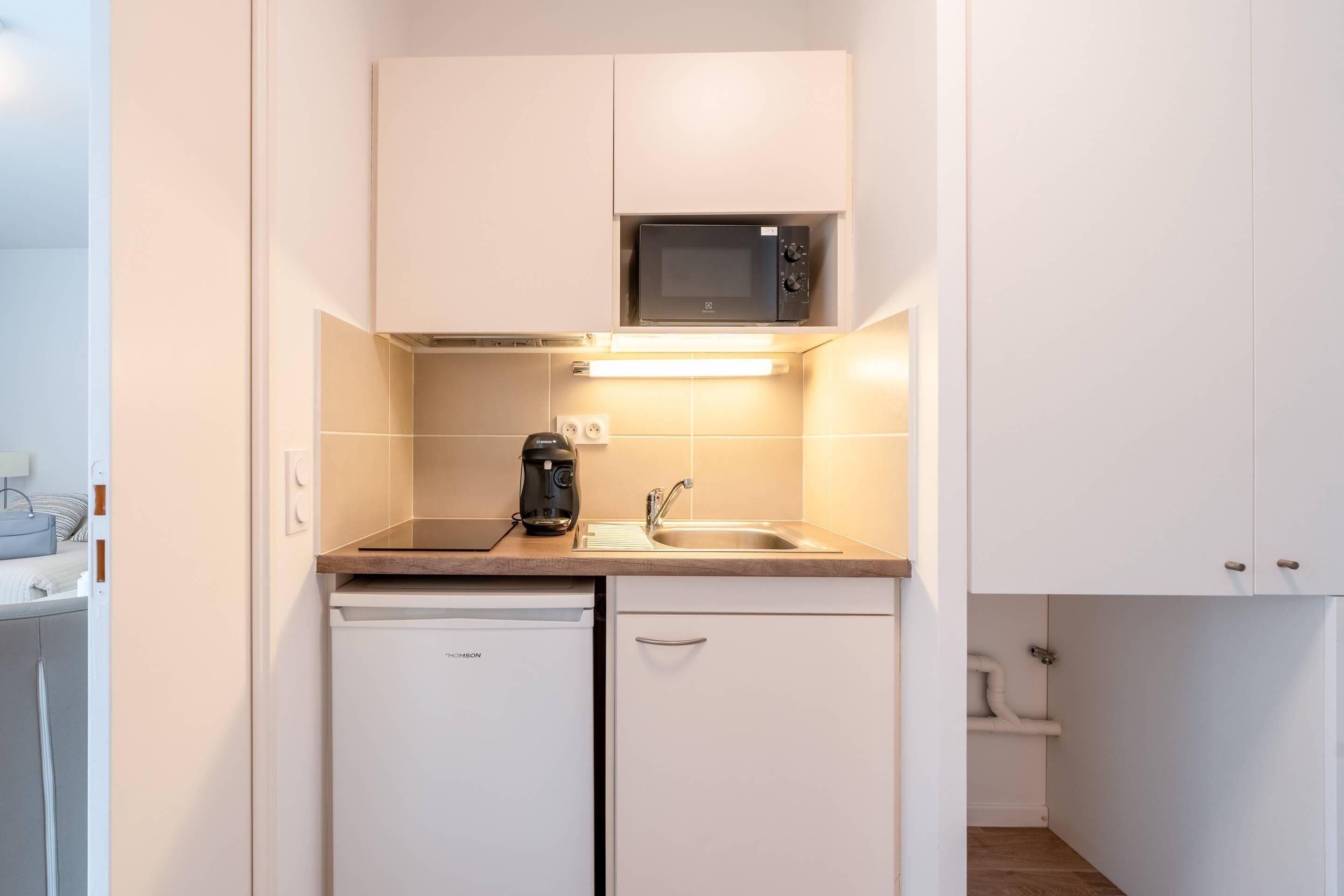 Een kleine keuken met een magnetron, koffiezetapparaat, spoelbak en vaatwasser.