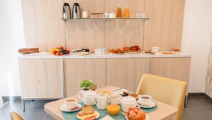 Ein Frühstückstisch mit verschiedenen Speisen und Getränken, ein Stuhl und eine Frühstückstheke mit weiteren Artikeln.